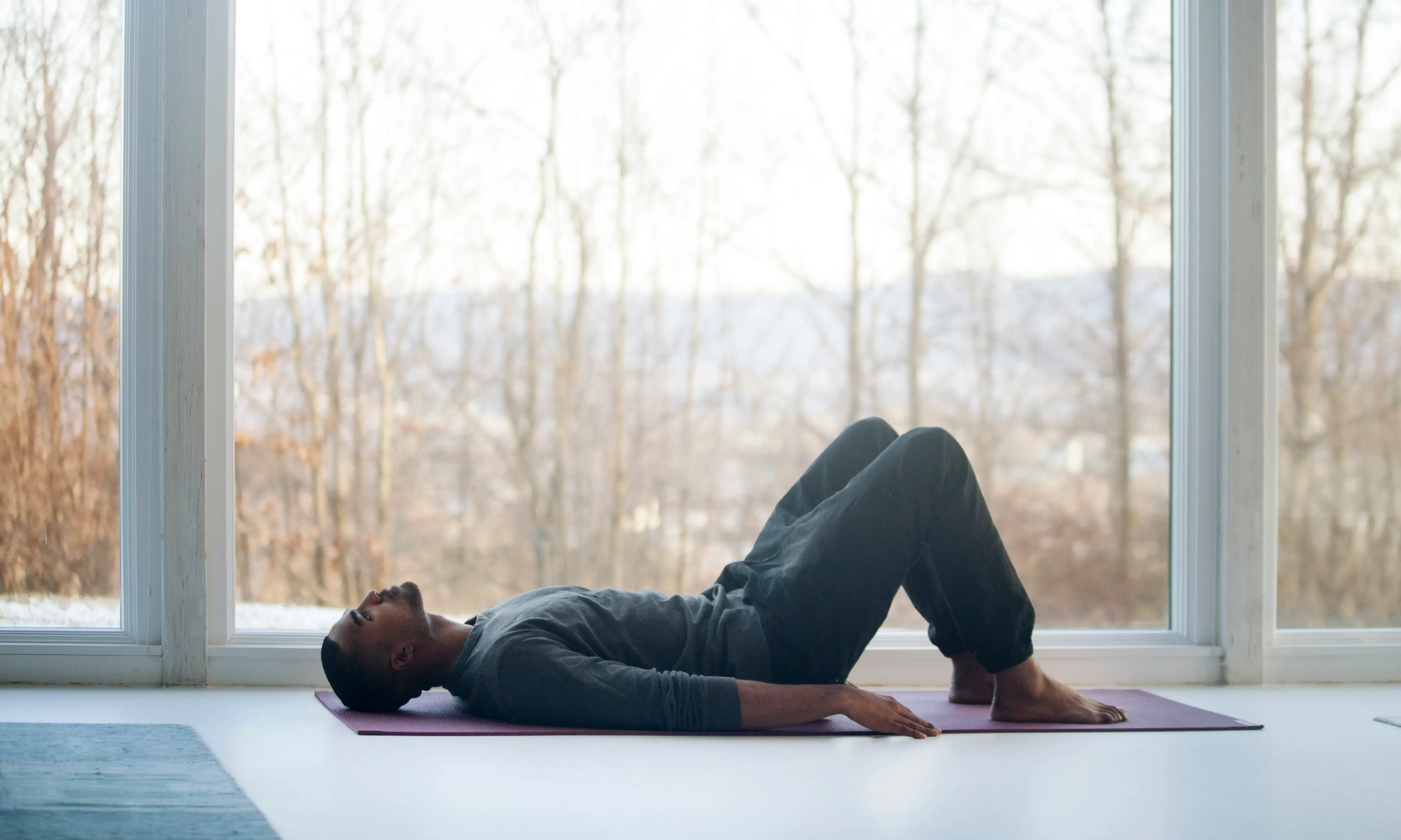 Mann liegt in grauer Kleidung auf Sportmatte