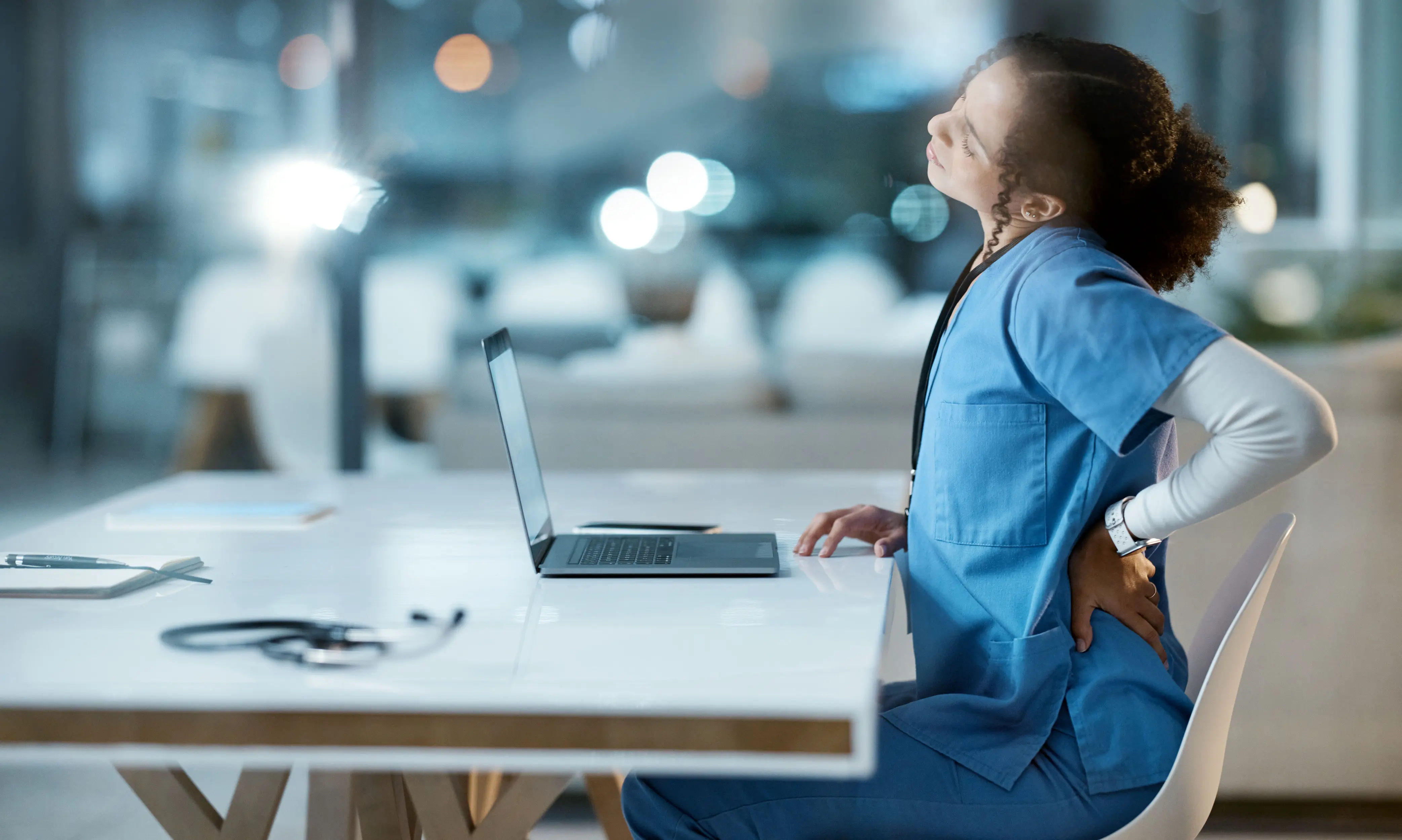 junge Frau am Laptop mit Rückenschmerzen