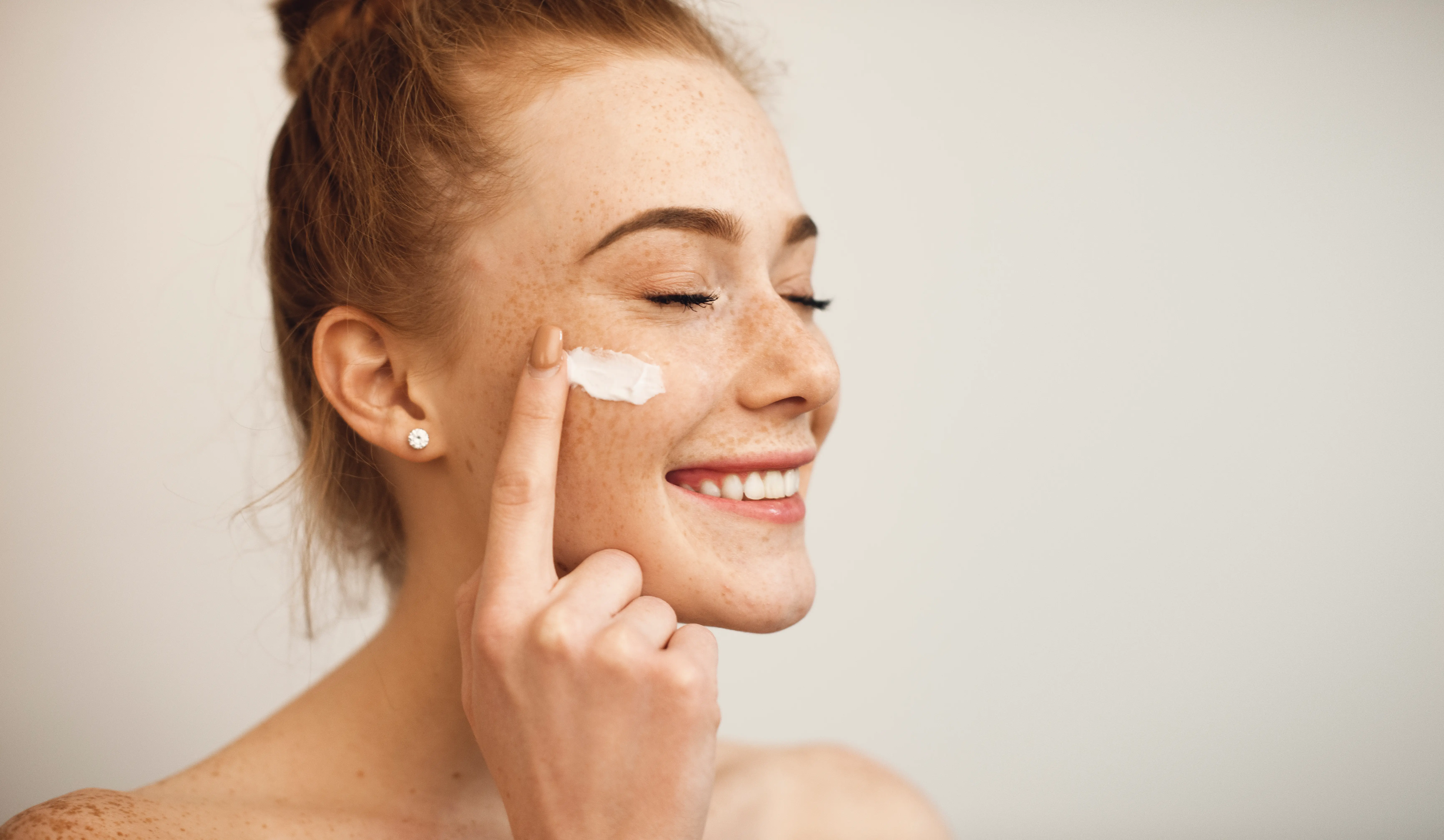 Junge Frau mit Sommersprossen und Creme im Gesicht Retinol